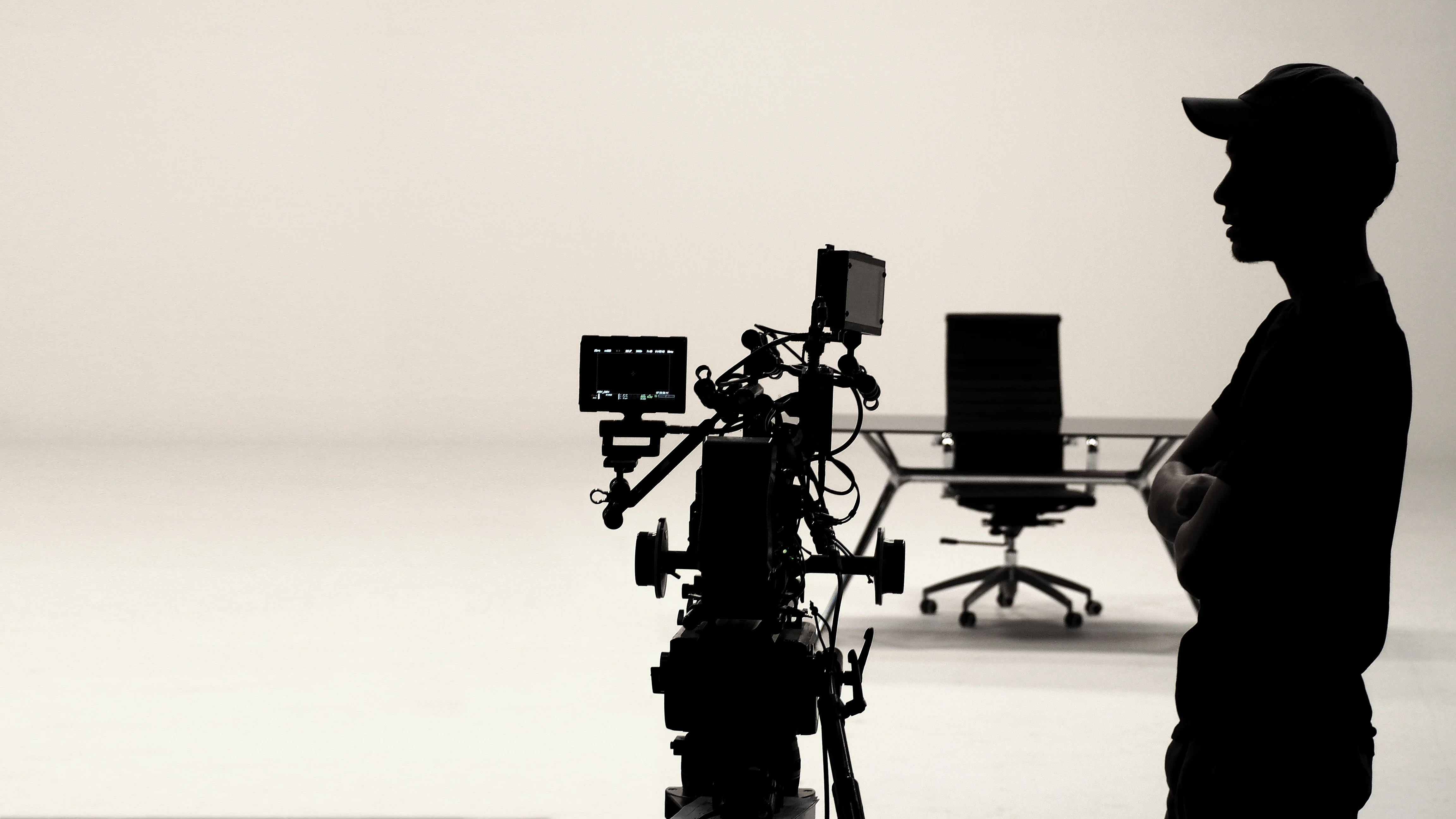 A camera operator beside a studio camera and an empty director's chair on a bright set